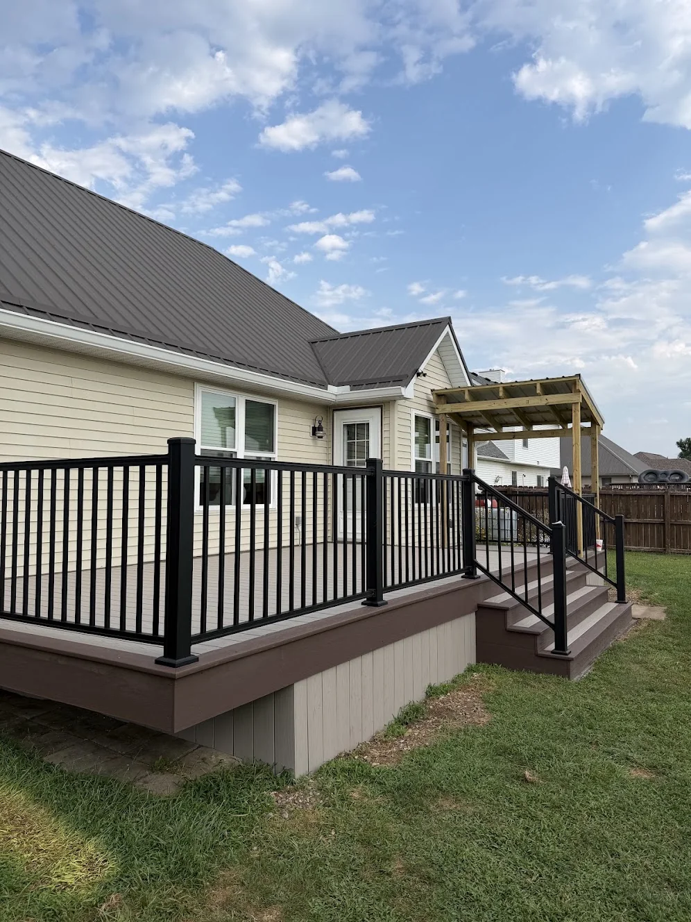 Deck with black railings and broad steps beside a home.