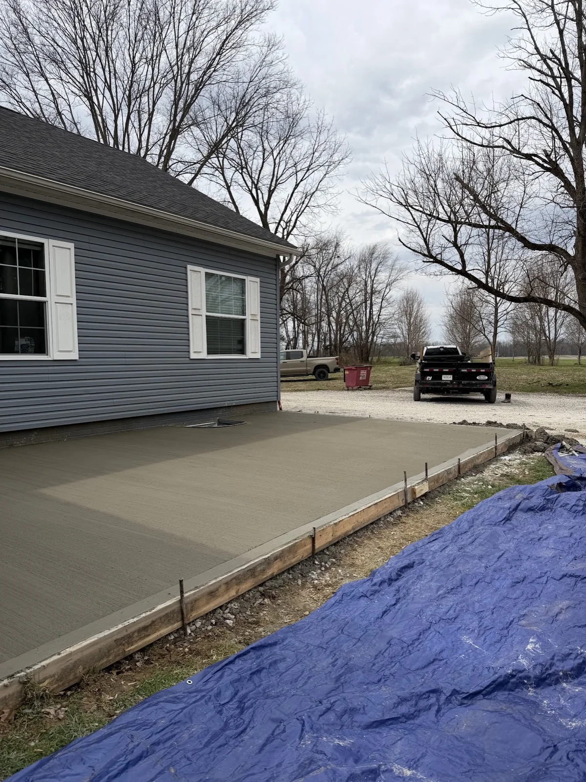 Freshly finished broom-textured concrete patio still in its forms beside a blue-gray house.