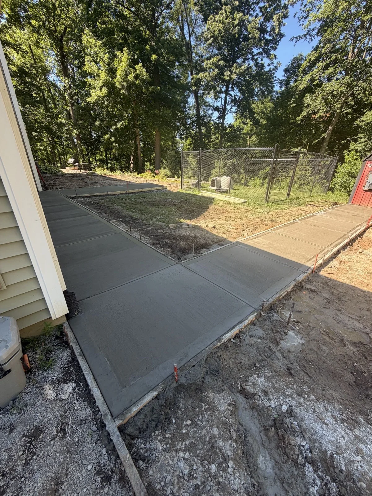 Freshly finished concrete sidewalk and pads still in forms, wrapping around a house toward a fenced backyard.