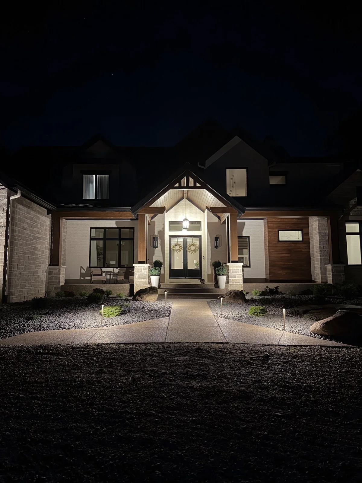 Dramatic nighttime view of a custom home entry with new path lights, rock beds, and boulders lining the front walkway.