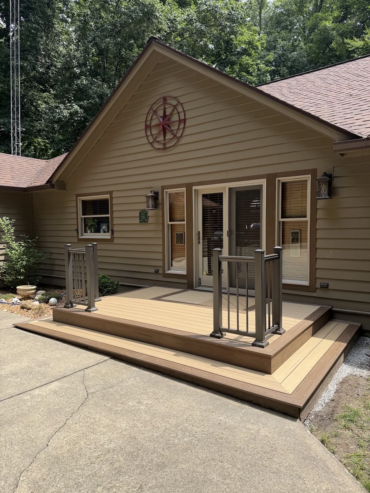 Wide view of a completed two-tone composite entry deck with wrap-around steps and railings on a gabled tan house.